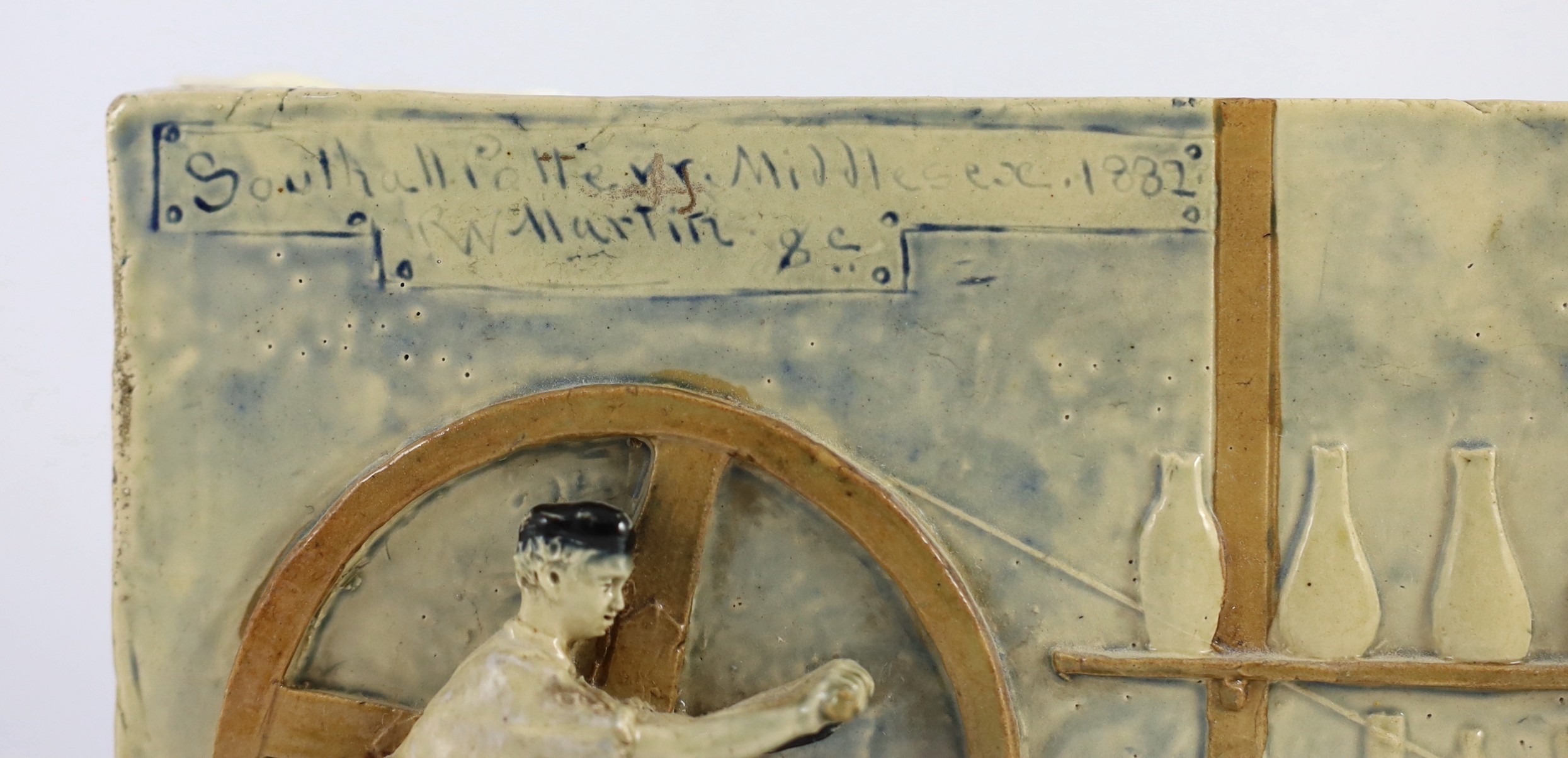 A rare Martin Brothers 'Wheel Boy, Bench Boy and Thrower' stoneware plaque, dated 1882, 41cm wide 17.5cm high